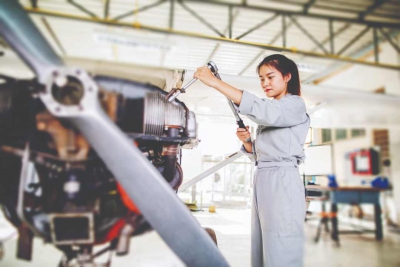 A woman in grey overalls holding a wrench and working on a car engine