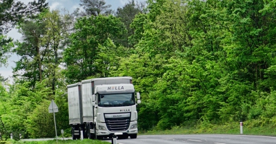 A white hella lorry drives down a road bordered by green trees