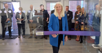 A woman about to cut the ribbon to open a new office with several people behind her