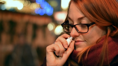 A lady with red air and black glasses using a nasal spray