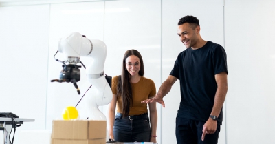 a man and a woman look at a white robot and smile
