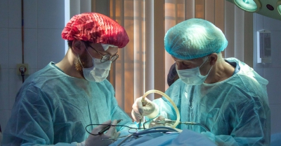 two surgeons with green ppe operate on a patient