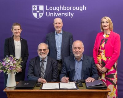 5 people signing an agreement in front of a Loughborough University background